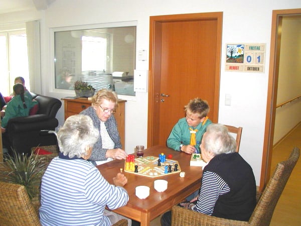 Eine Gruppe Senioren spielt mit einem jungen Besucher ein Brettspiel.